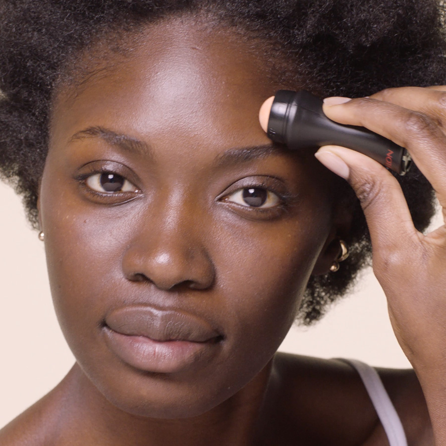 Closeup of woman using oil-absorbing roller on forehead. 